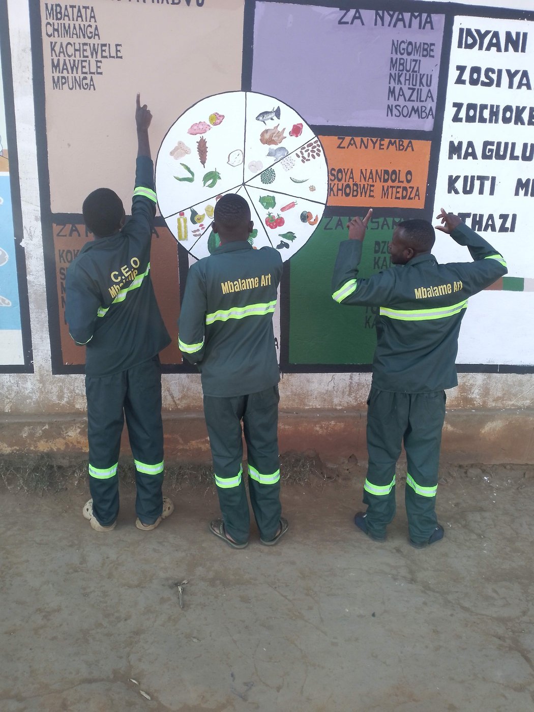 Mbalame Art team in branded uniforms reviewing a completed mural
